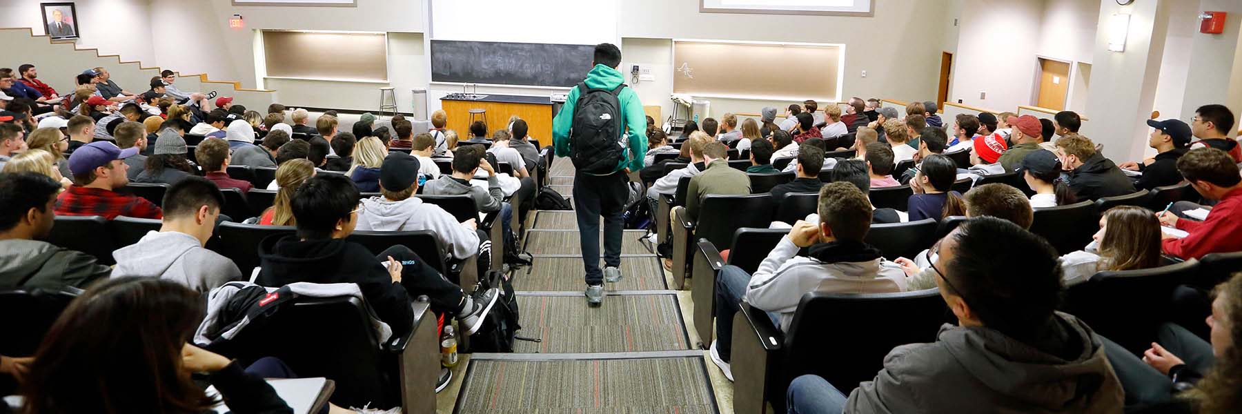 A student walks down the stairs to join his class in a large lecture hall.